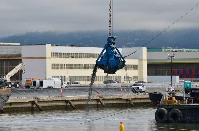 Dredging the northwest corner of the Seaplane Lagoon at Alameda Point in February 2012.  Tarmac dewatering, drying, and testing area behind black tarp is now being dismantled.  All dredging work is completed. 