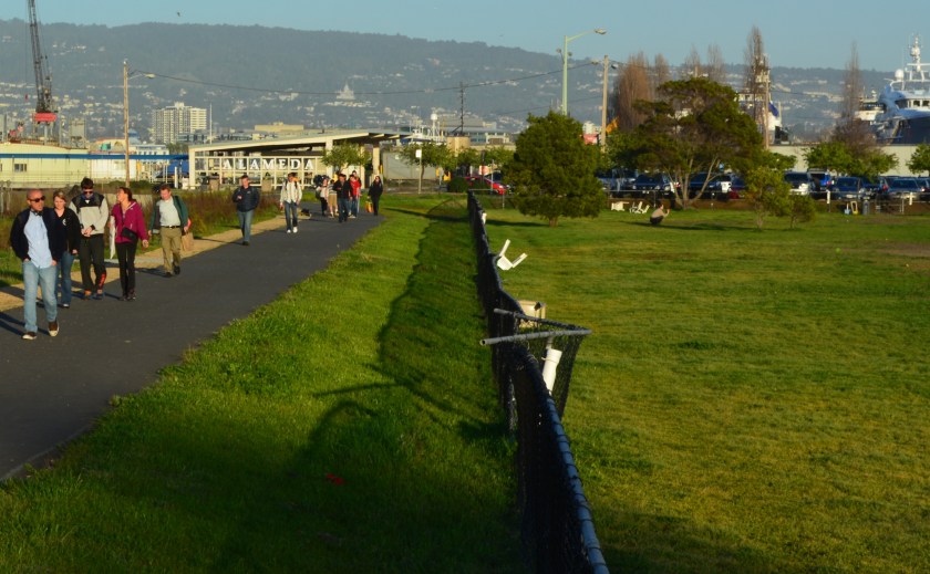 Ferry riders leaving the Main Street Ferry Terminal in the background and walking toward makeshift parking lot.  Dog park is on the right. 